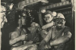 Es handelt sich um eine Schwarz-Weiß-Fotografie. Auf dieser sind fünf Männer abgebildet. Sie sitzen in einem Abbauort unter Tage und schauen zum Teil in die Kamera. Ihre Gesichter und ihre nackten Oberkörper sind von Kohlenstaub verschmutzt. Die Bergleute haben Schutzhelme mit aufgesteckten Lampen auf.
