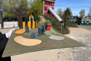 Im Vordergrund befindet sich ein vereinfachtes Modell eines Spielplatzes, in dessen Zentrum eine kleine Version des Förderturms zu sehen ist. Im Hintergrund ist ein Teil des Spielplatzes der Kohlewelt abgebildet.