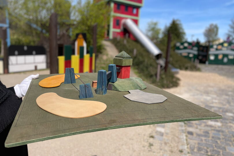 Im Vordergrund befindet sich ein vereinfachtes Modell eines Spielplatzes, in dessen Zentrum eine kleine Version des Förderturms zu sehen ist. Im Hintergrund ist ein Teil des Spielplatzes der Kohlewelt abgebildet.